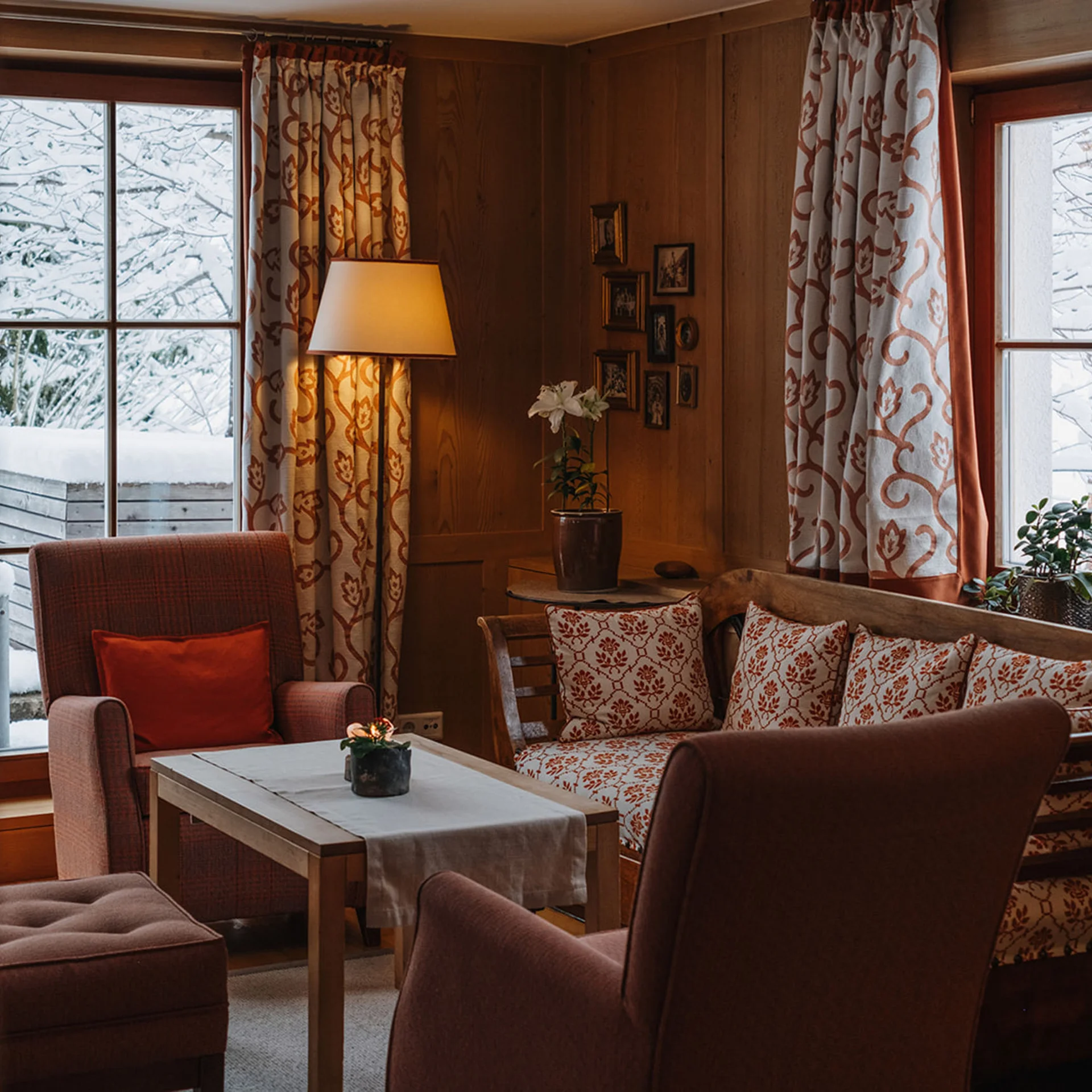 Gemütliches Wohnzimmer mit Holzwänden, Sessel und Schneeblick außen