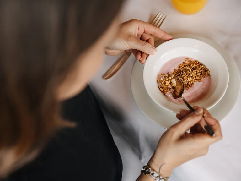 Frau isst Müsli mit Joghurt aus einer weißen Schüssel am Tisch