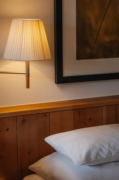 Wandlampe über Holzkopfteil und weißen Kissen in einem Schlafzimmer