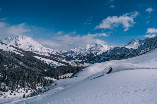 Snowboarder fährt die Piste runter mit einem wunderschönen Panorama über Lech