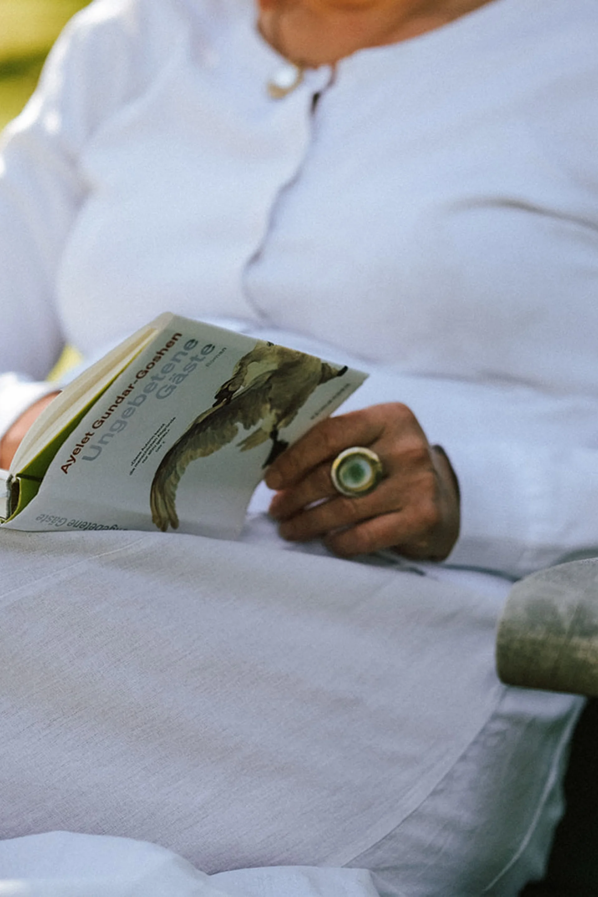 Person in weißem Kleid liest Buch im Garten
