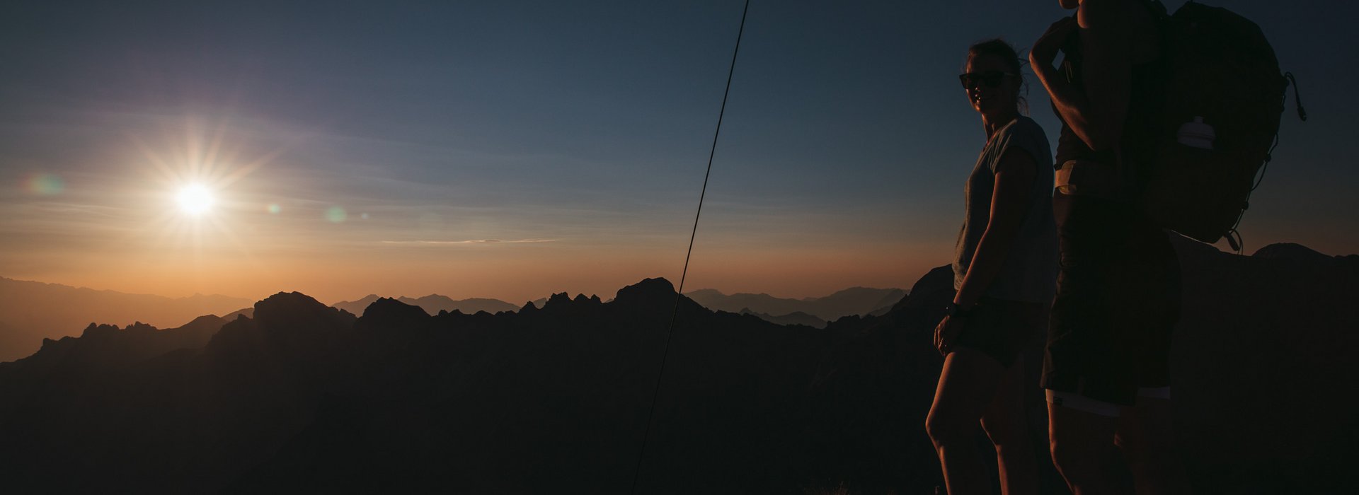 Zwei Personen am Gipfel schauen den Sonnenuntergang zu. 