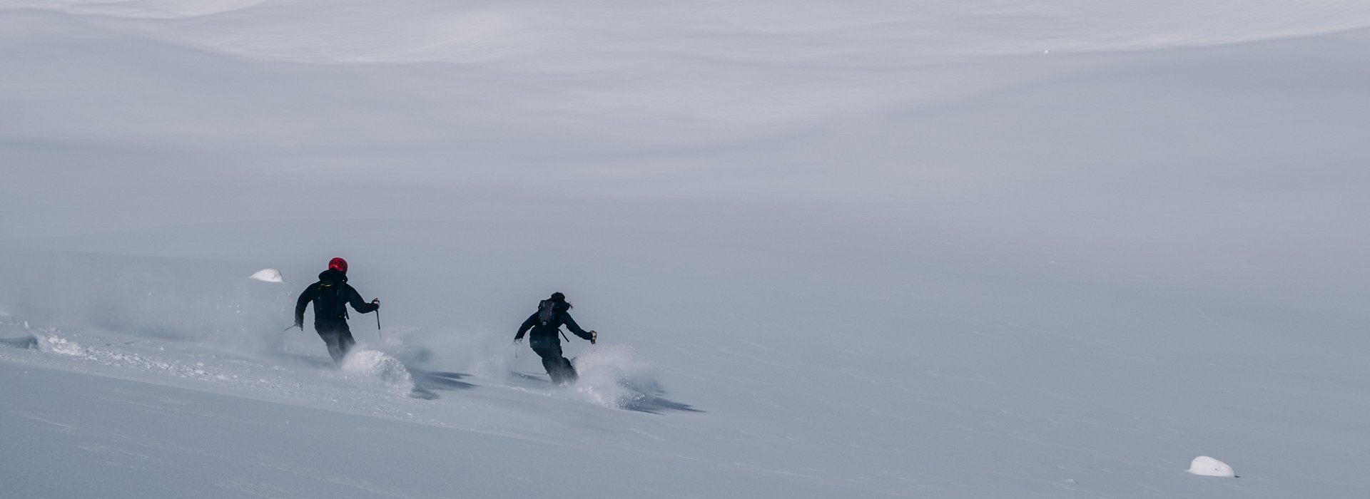 Zwei Skifahrer fahren Off-Pist über die weiße Schneelandschaft.
