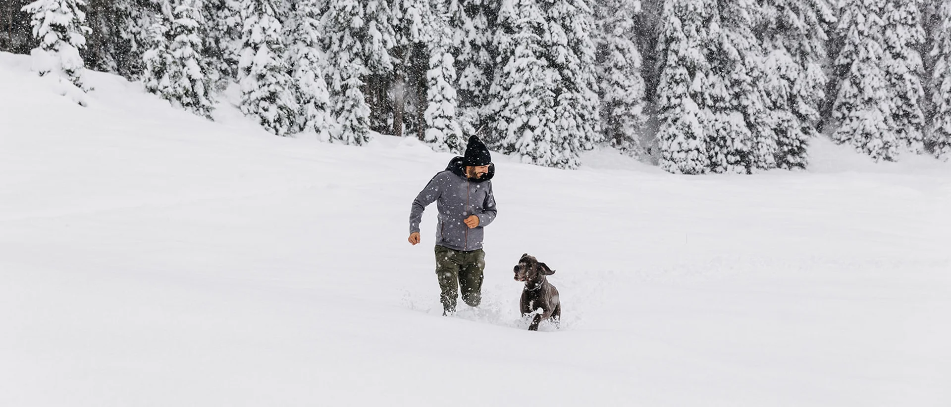 Mann joggt mit Hund im tiefen Schnee vor verschneiten Bäumen