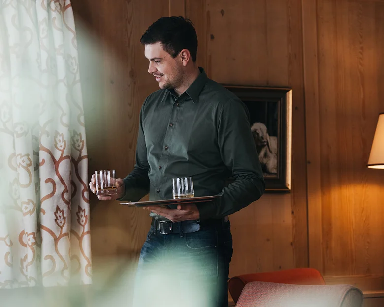 Das Team des Hotel Aurora in Lech Mann trägt Tablett mit zwei Gläsern in gemütlichem Wohnzimmer