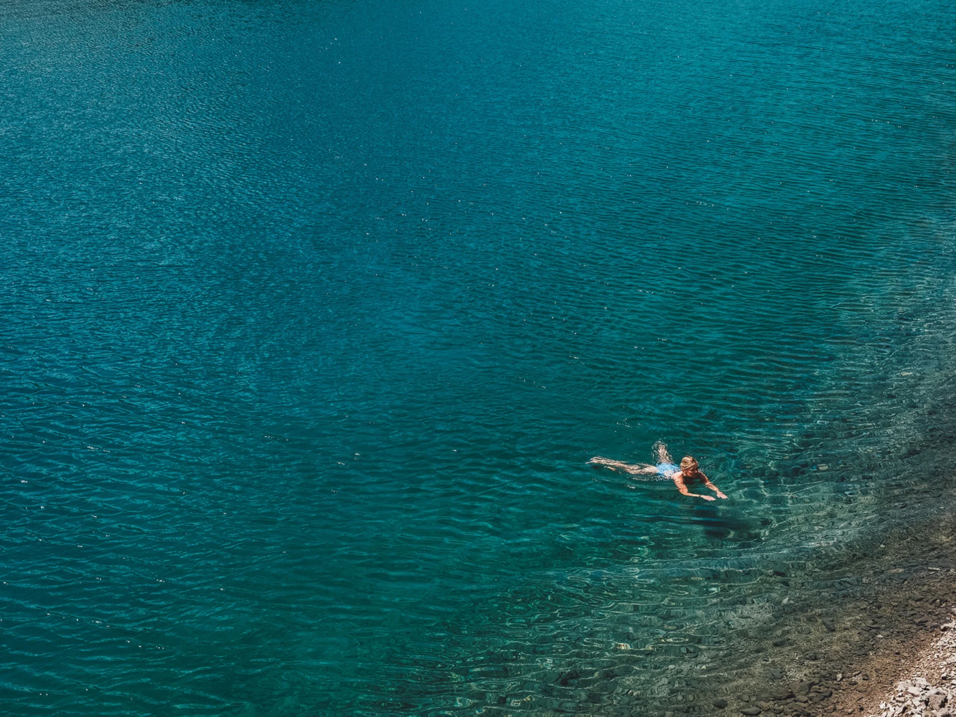 Person swimming in clear blue water near a rocky shore