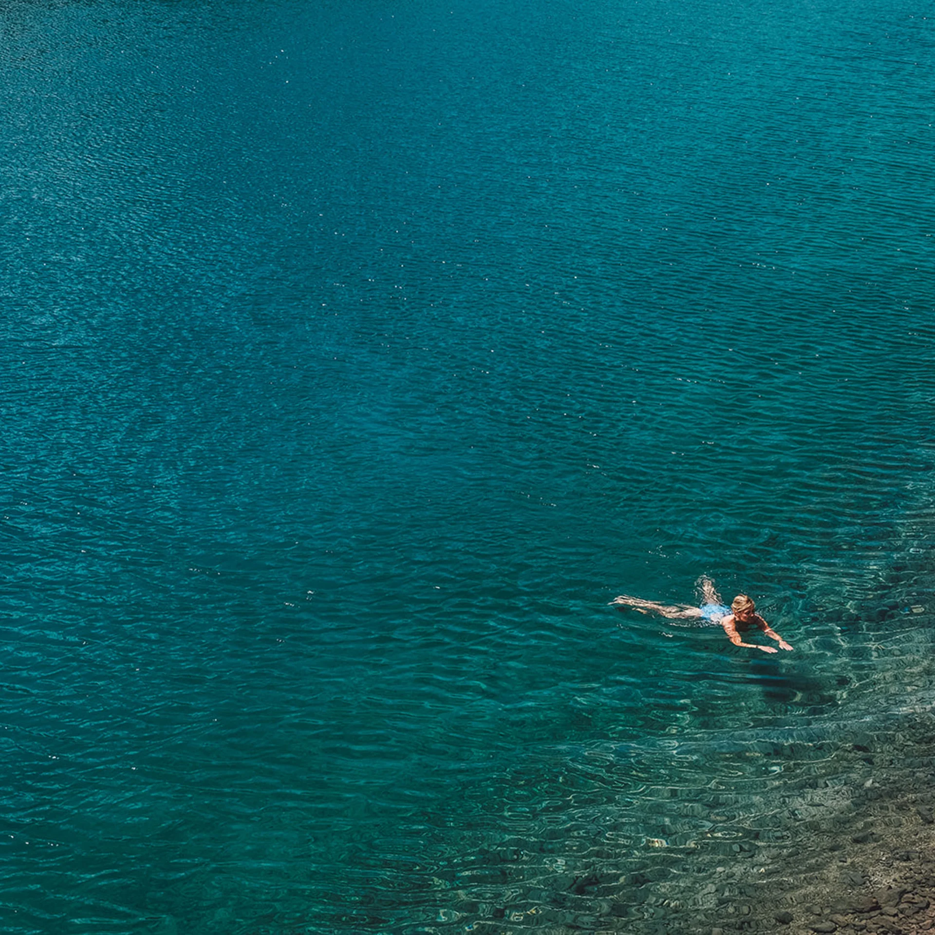 Person schwimmt im klaren blauen Wasser an einem felsigen Ufer