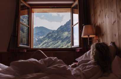 Dame blickt aus dem offenen Fenster auf die Lecher Bergwelt.