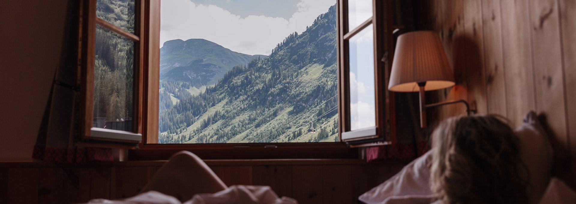 Dame blickt aus dem offenen Fenster auf die Lecher Bergwelt.