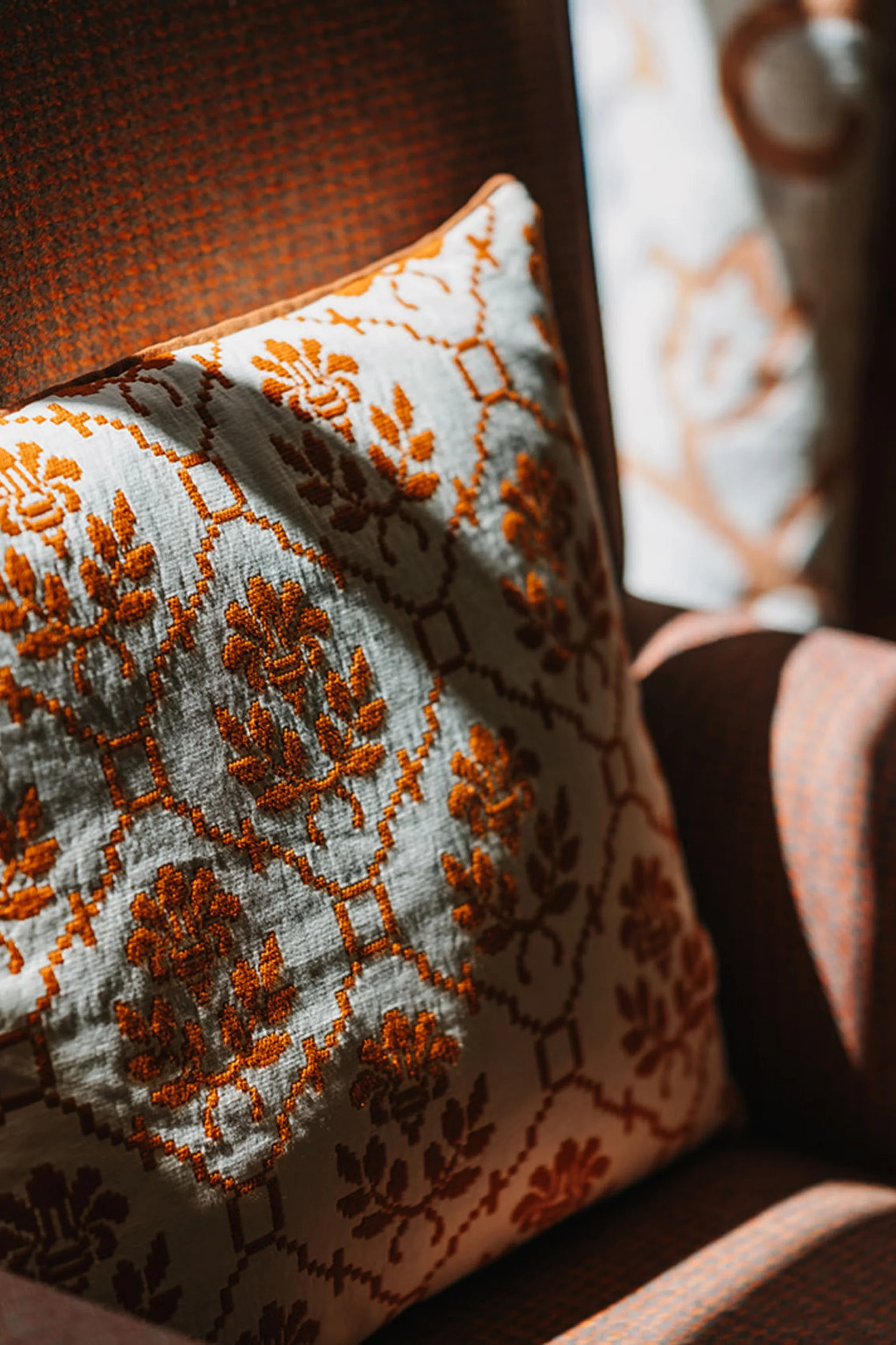 Gemusterter Kissenbezug auf braunem Stuhl bei Sonnenlicht