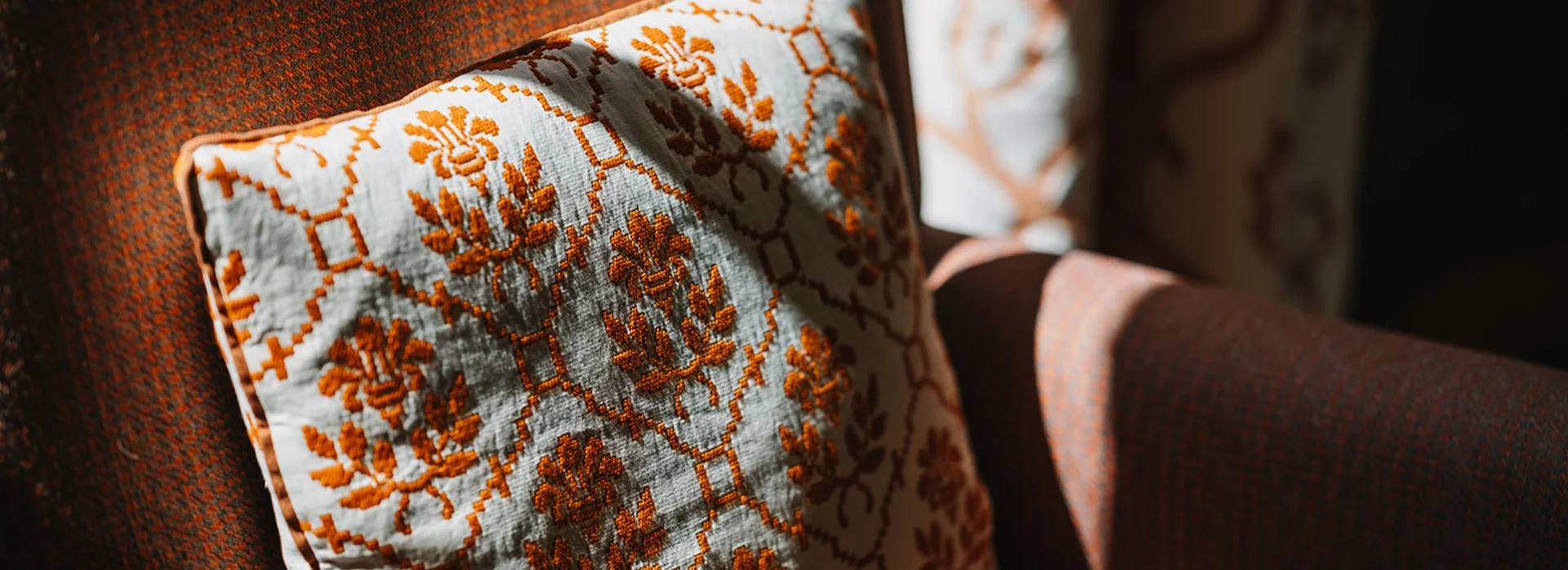 Gemusterter Kissenbezug auf braunem Stuhl bei Sonnenlicht