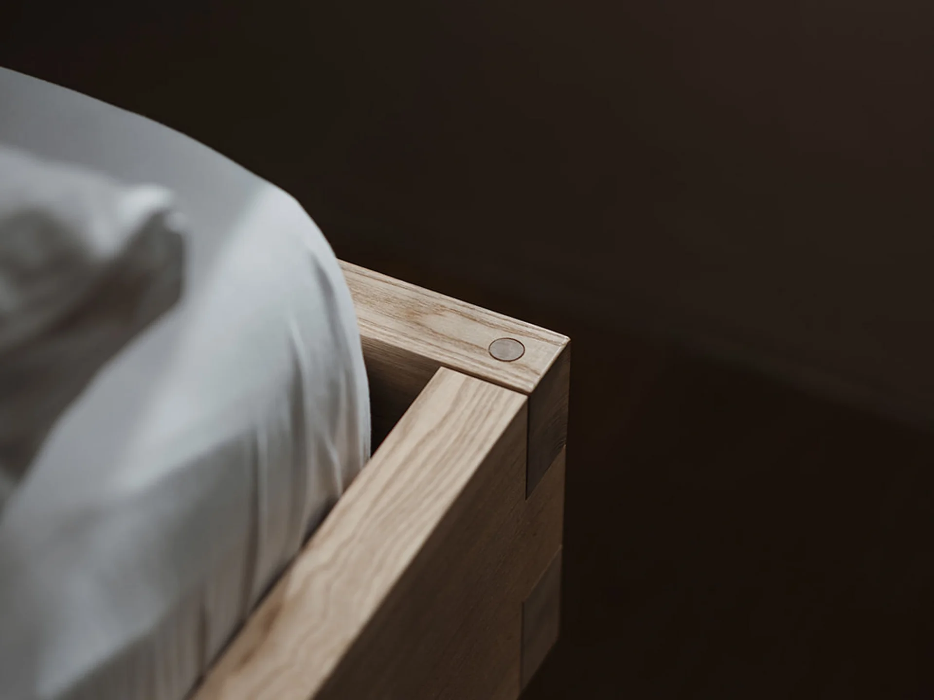 Corner view of a modern light wood bed frame with white mattress