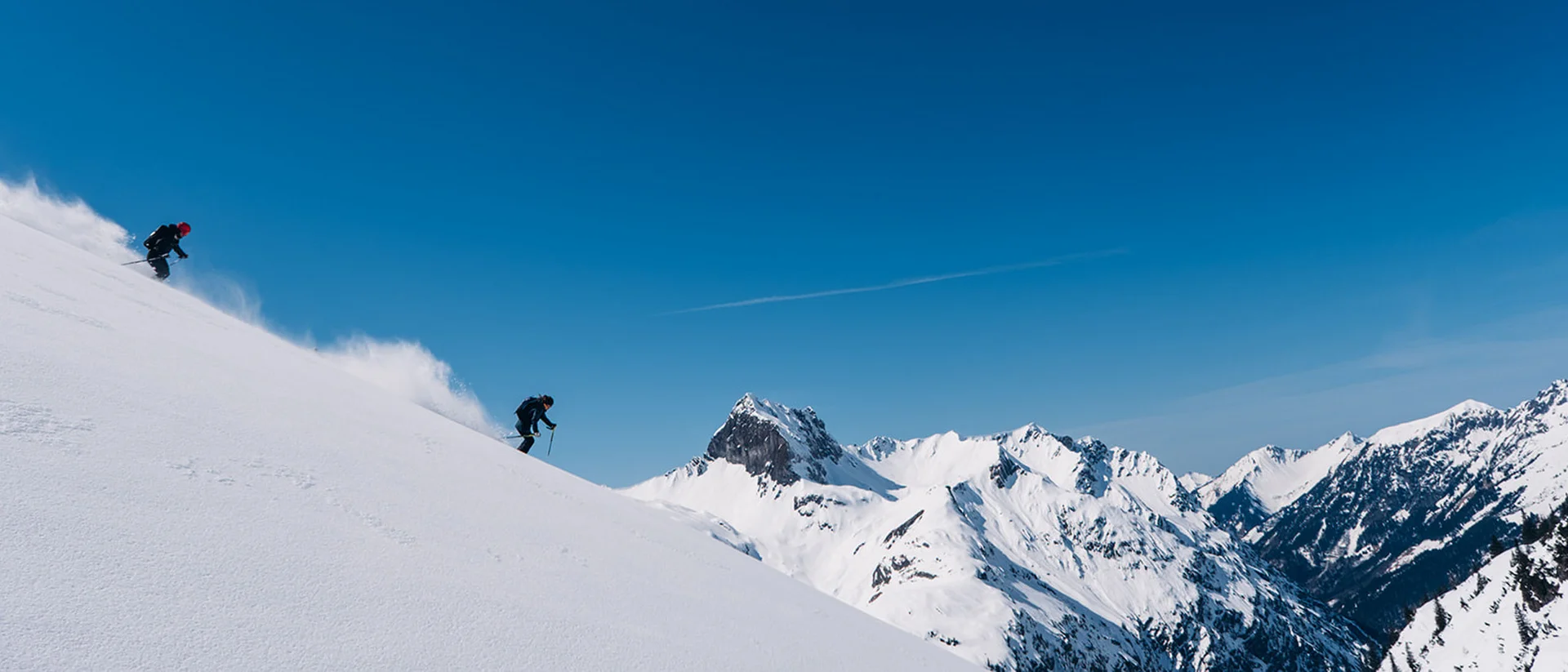 Winterurlaub in Lech am Arlberg im Hotel Aurora Zwei Skifahrer fahren einen verschneiten Berg bei klarem Himmel hinunter