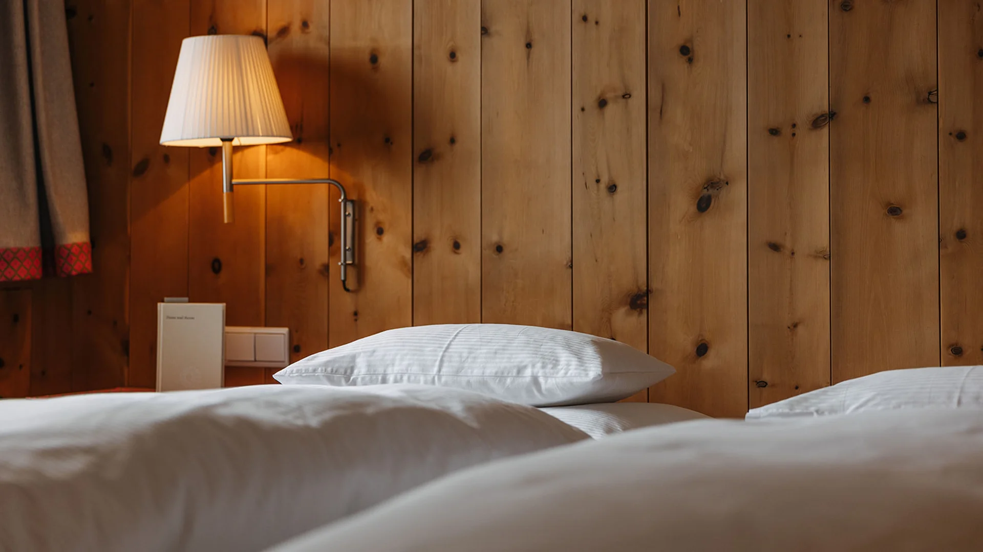 Weißes Bett mit Kopfkissen und Wandlampe an Holzwand