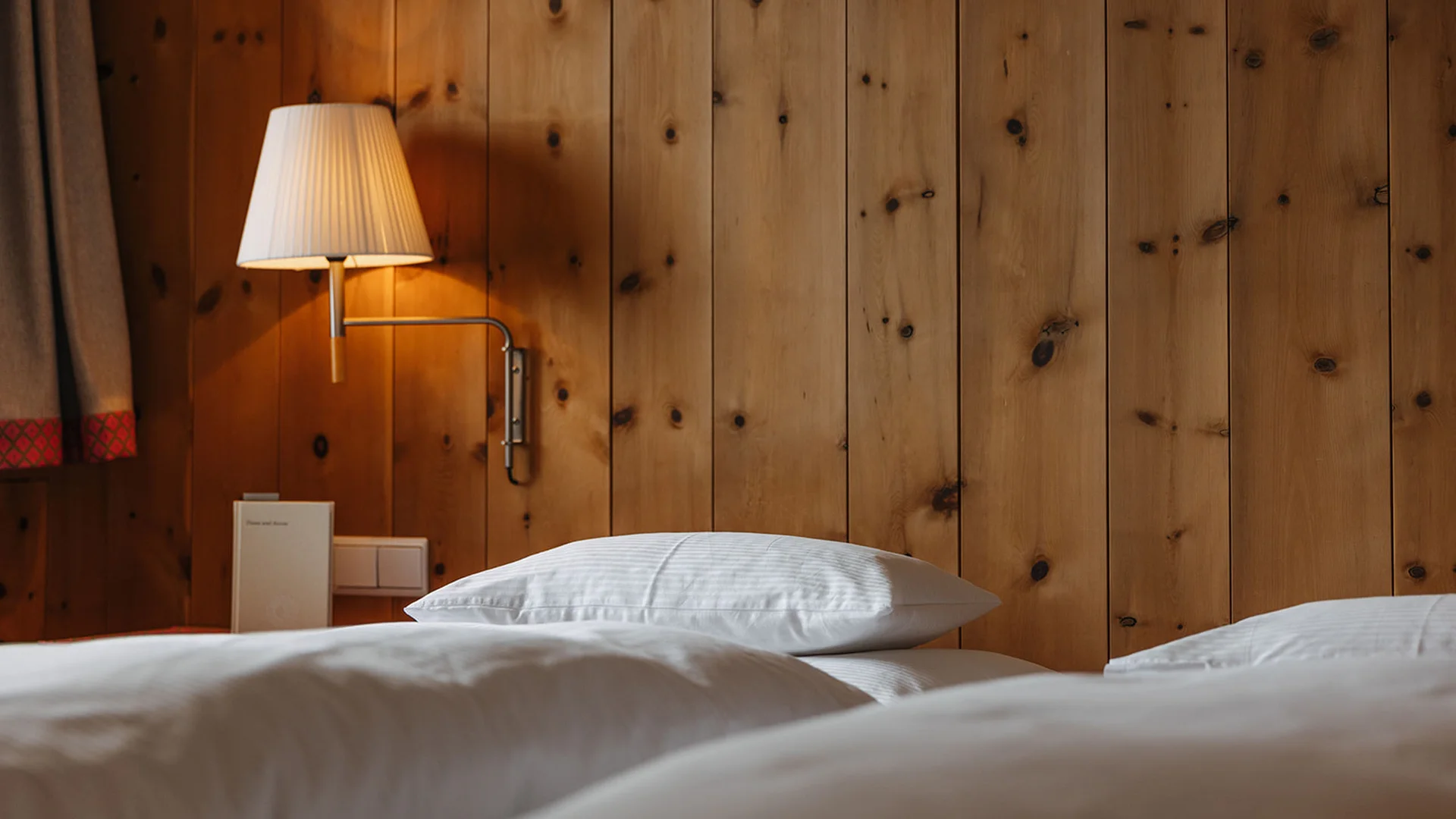 Weißes Bett mit Kopfkissen und Wandlampe an Holzwand