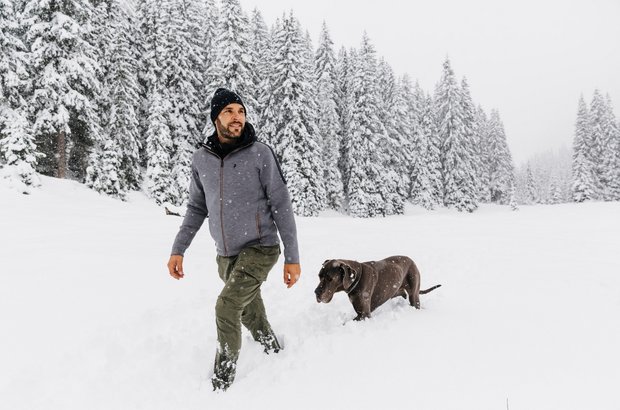 Hund geht mit seinem Herrchen durch die Winterlandschaft