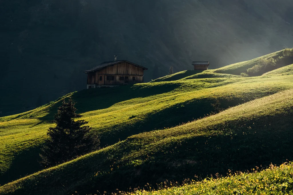 Sonnenbeschienene grüne Hügel mit zwei Holzhütten in den Bergen