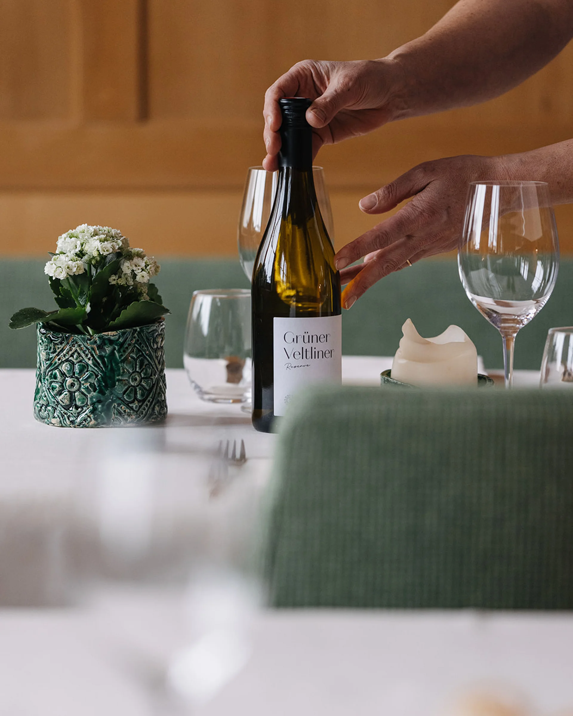Person stellt Weinflasche Grüner Veltliner auf gedeckten Tisch mit Gläsern