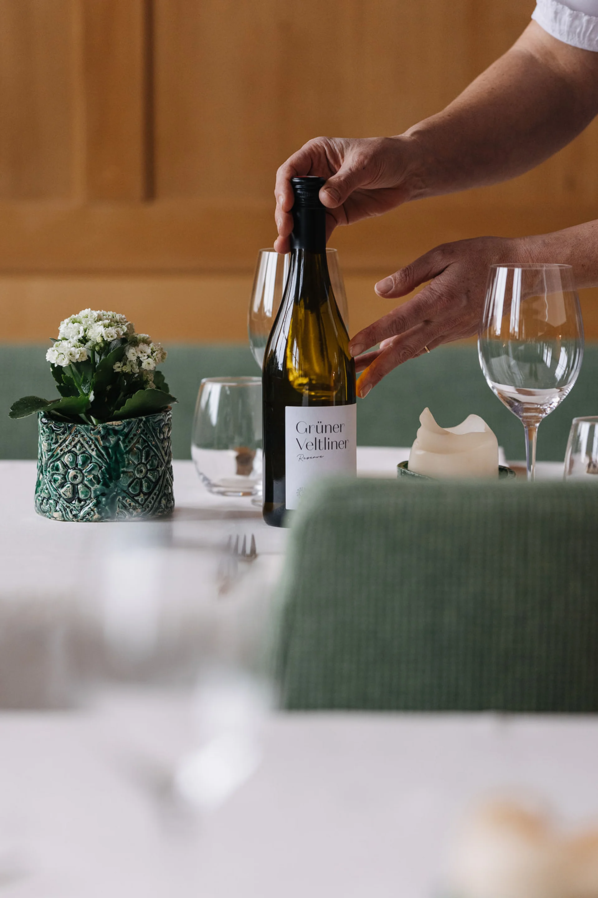 Person stellt Weinflasche Grüner Veltliner auf gedeckten Tisch mit Gläsern