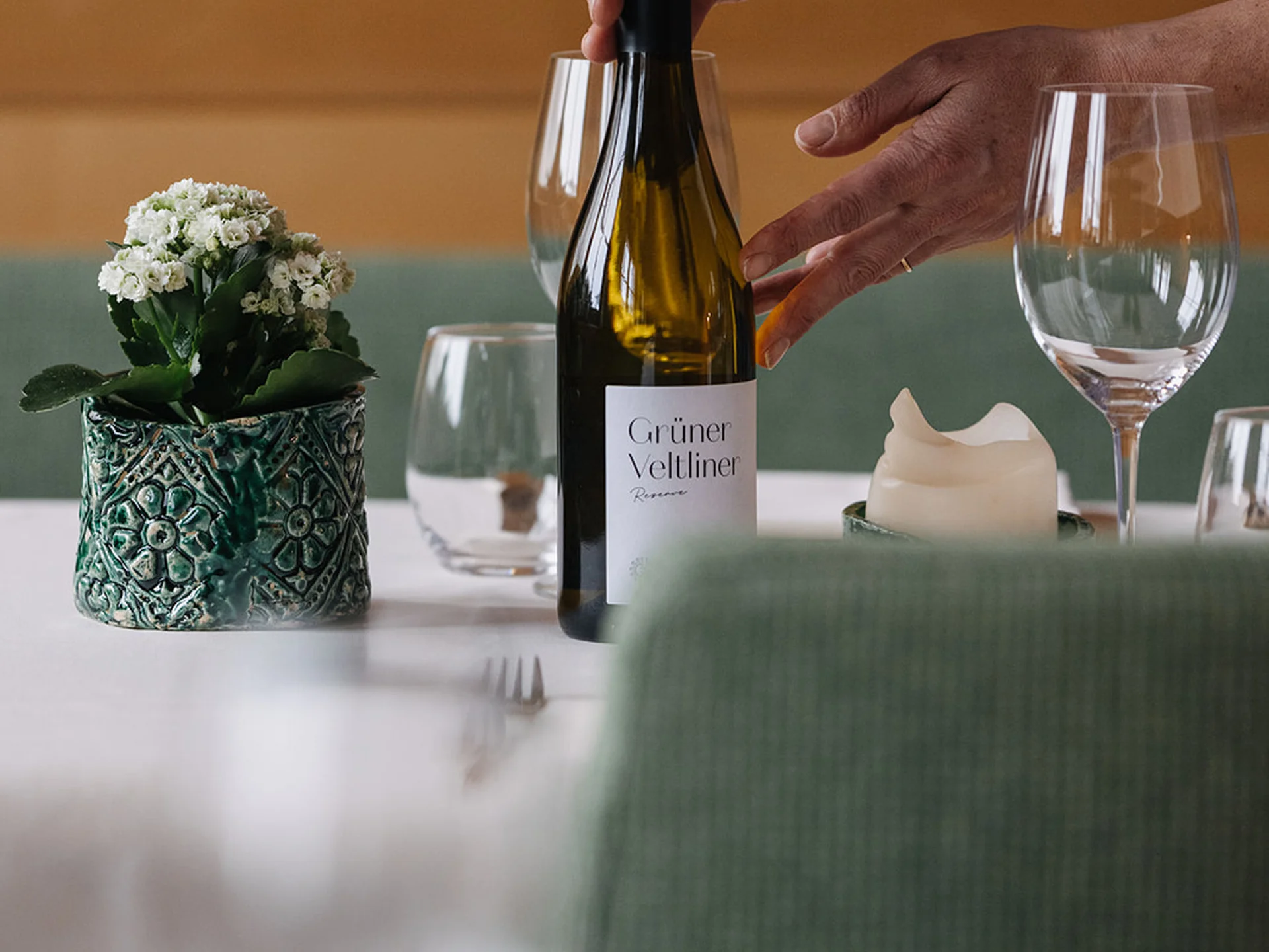 Person placing Grüner Veltliner wine bottle on set table with glasses