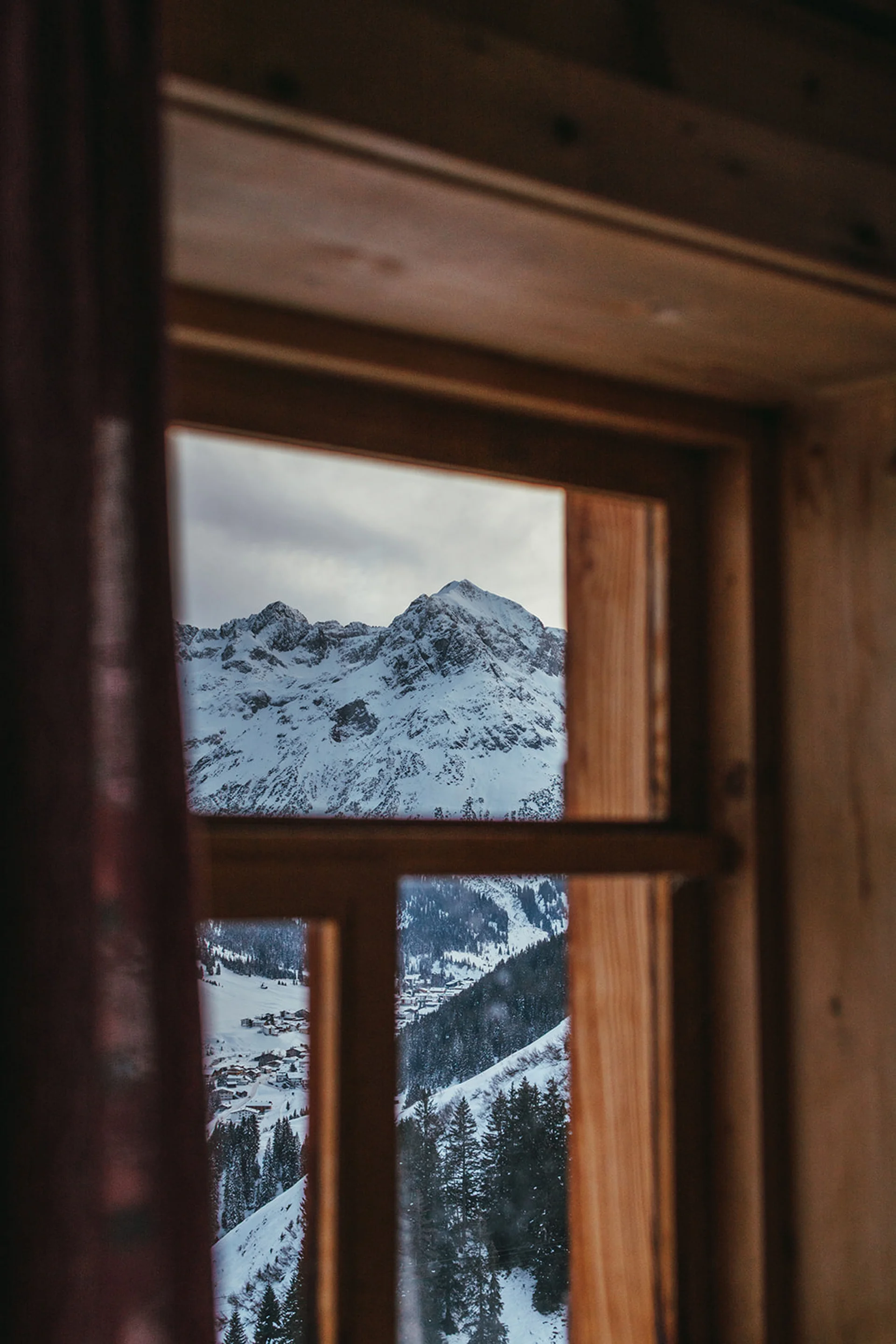 Blick aus Holzfenster auf schneebedeckte Berge und Wälder