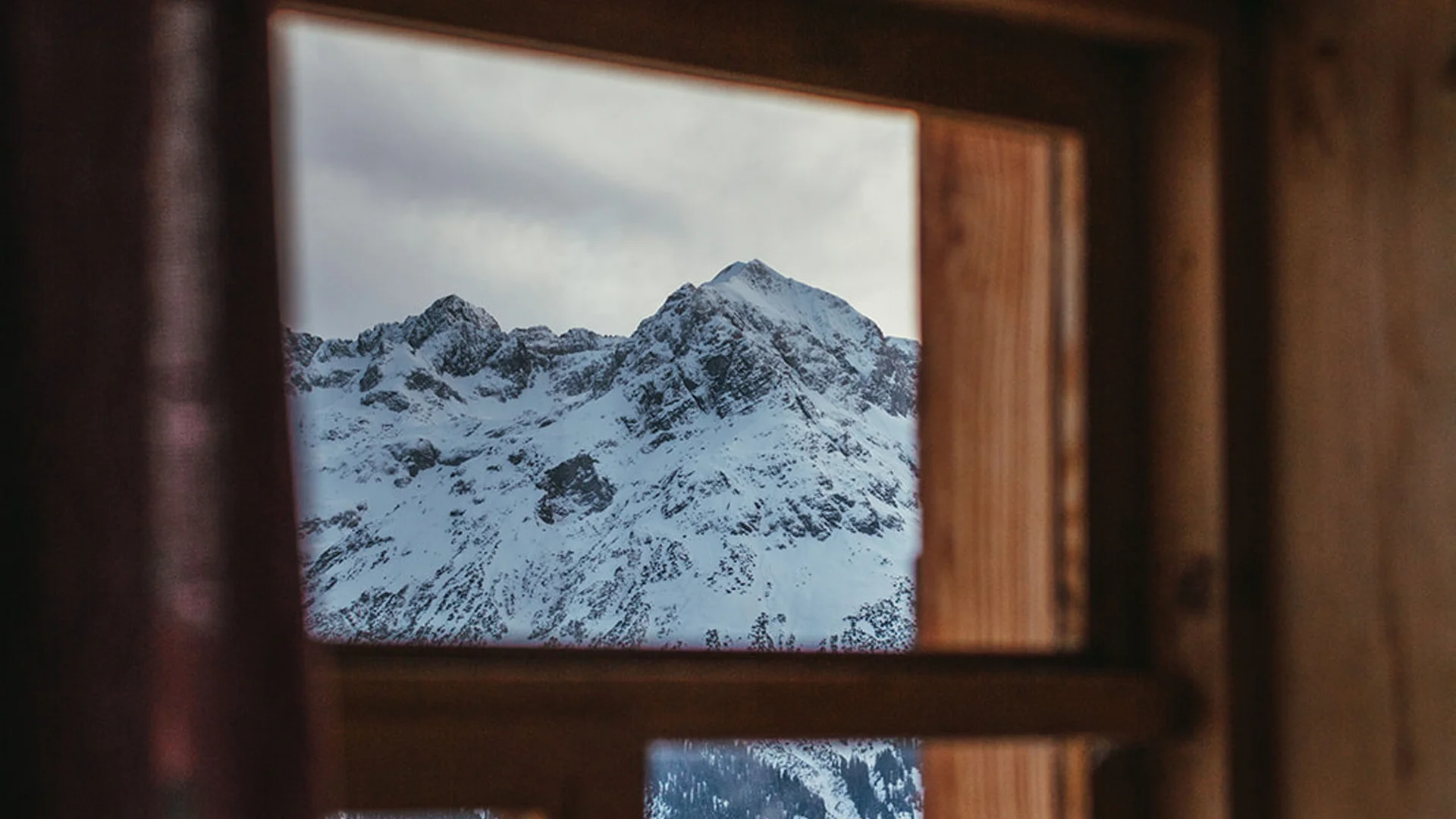 Blick aus Holzfenster auf schneebedeckte Berge und Wälder