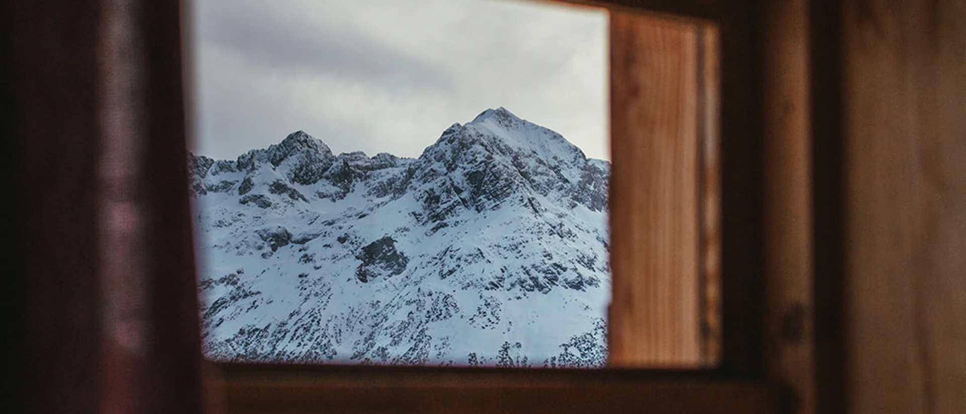 View through wooden window of snow-covered mountains and trees