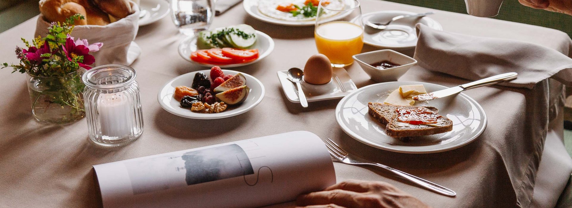 Frühstückstisch gedeckt mit frischem Obst, Brot, gekochtes Ei, Kaffee und frisch gepresstem Orangensaft.