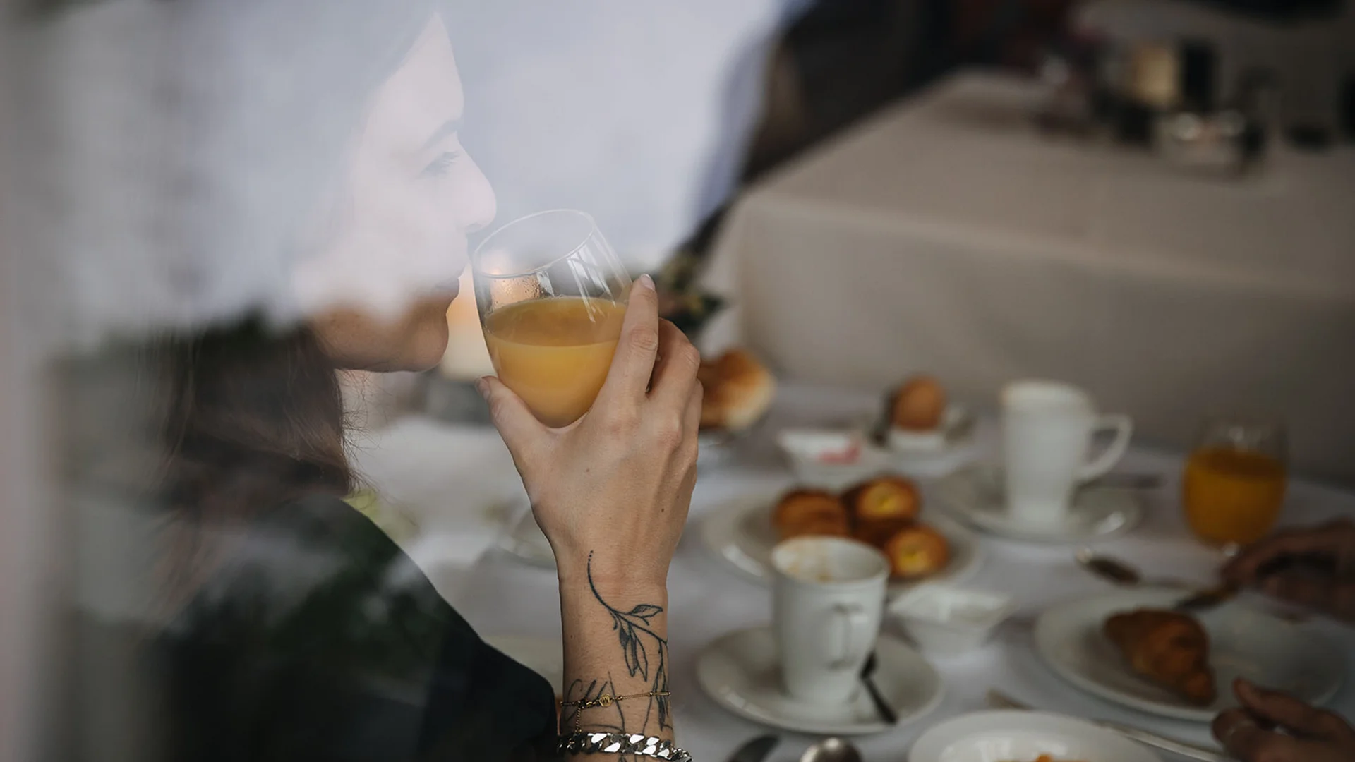 Frau trinkt Orangensaft beim Frühstück an einem gedeckten Tisch