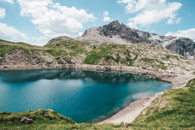 Diverse events set against a stunning mountain backdrop Mountain lake with clear blue water and rocky Alps under blue sky