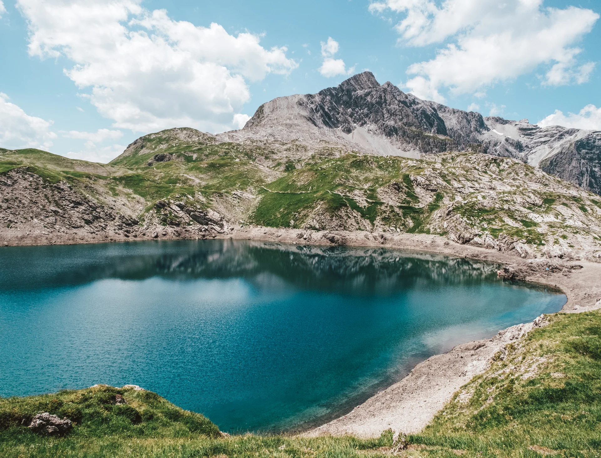 Diverse events set against a stunning mountain backdrop Mountain lake with clear blue water and rocky Alps under blue sky