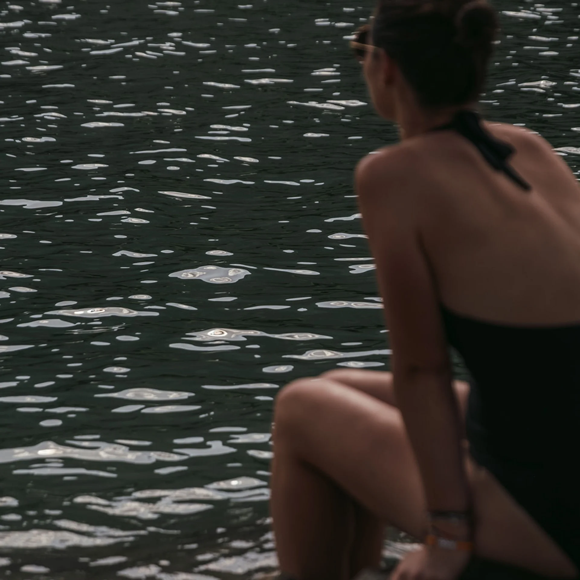 Frau im Badeanzug sitzt auf einem Felsen und blickt auf das Wasser