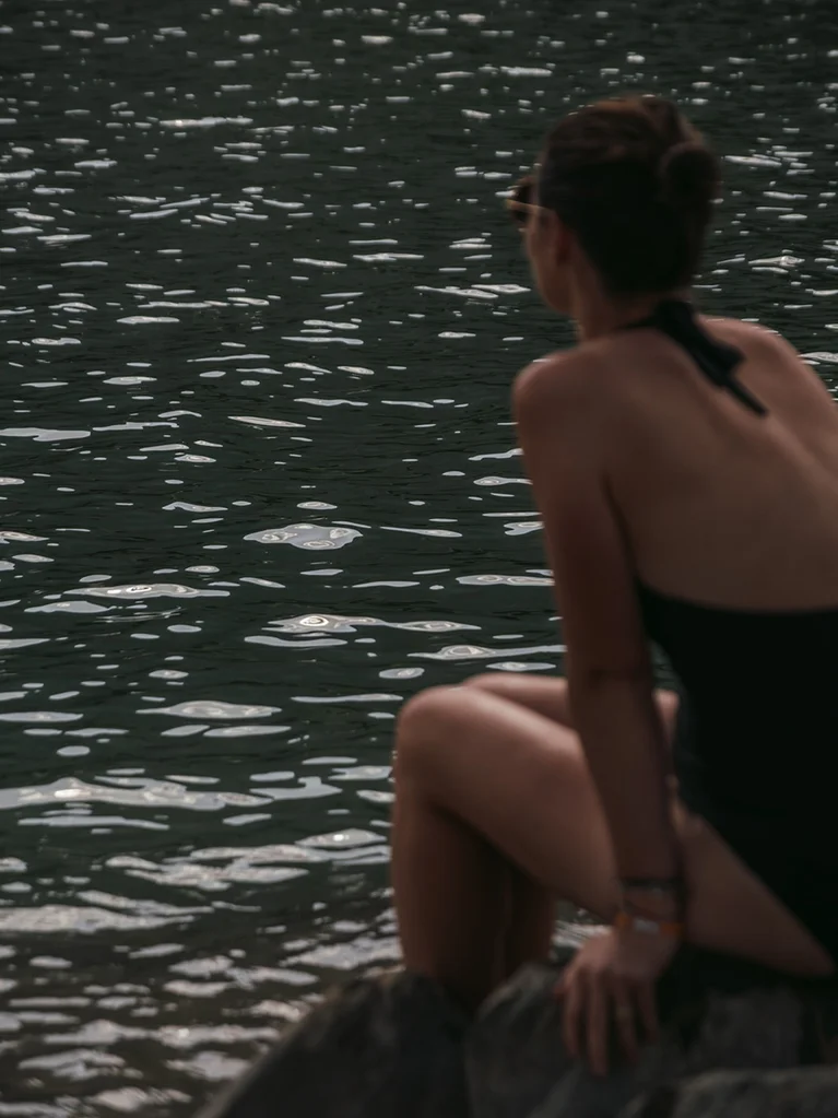 Woman in swimsuit sitting on rock looking at the water