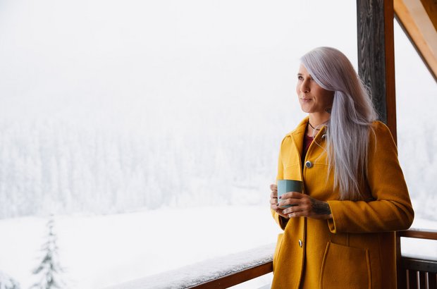 Frau am Balkon schaut in verschneite Winterlandschaft