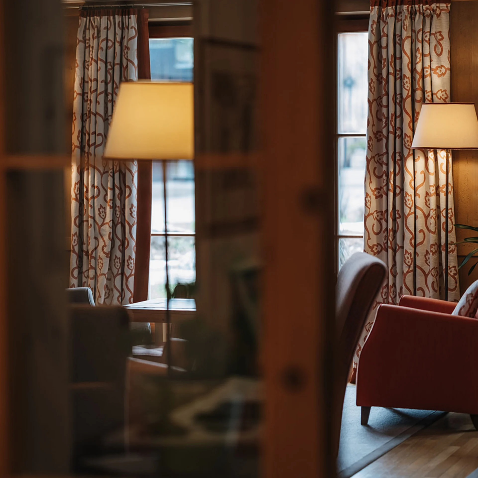 Gemütlicher Raum mit rotem Sessel, Lampe und gemusterten Vorhängen