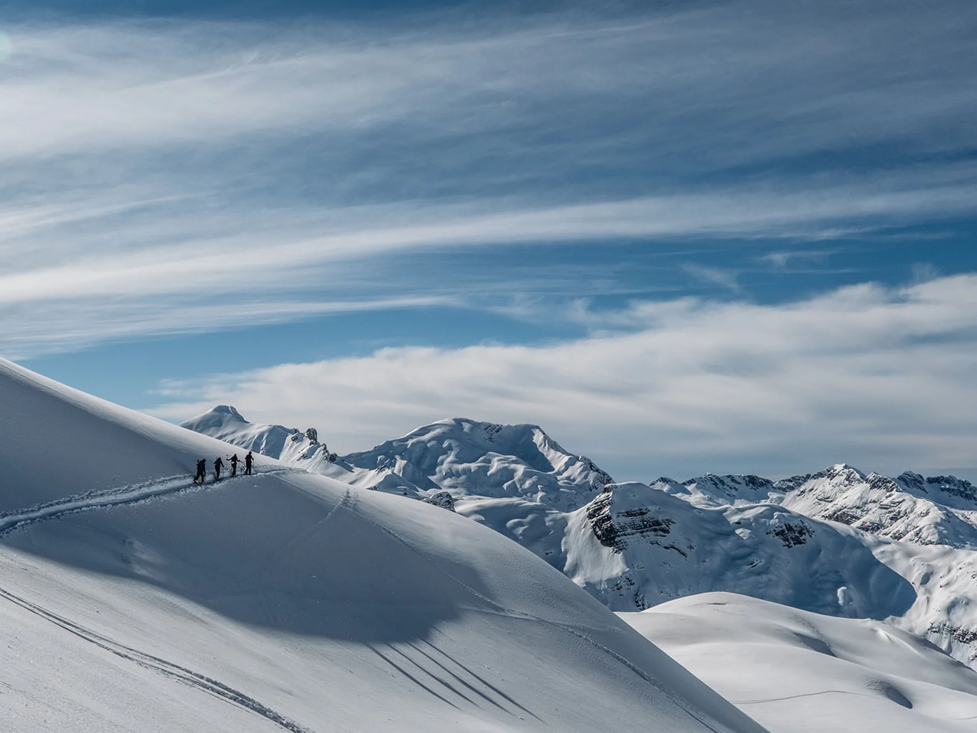 Group of hikers on a snowy mountain ridge with snowy peaks behind them