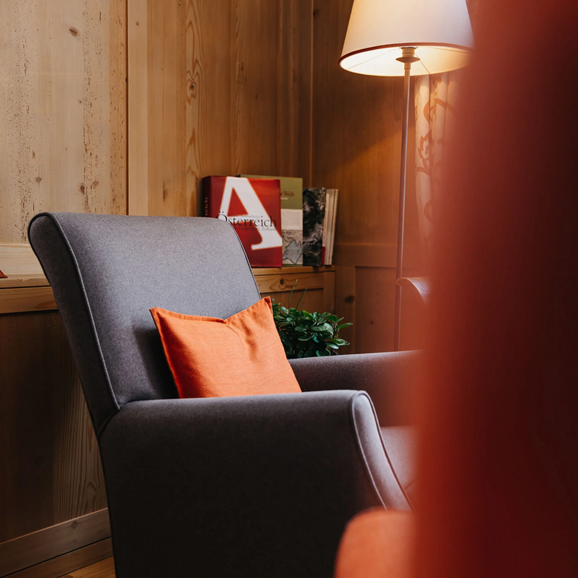 Gemütlicher Sessel mit orangenem Kissen in einem Holzraum mit Vorhängen und Lampe