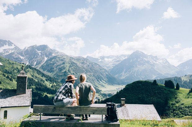 Zwei Personen sitzen auf einer Holzbank mit Ausblick in die Berge