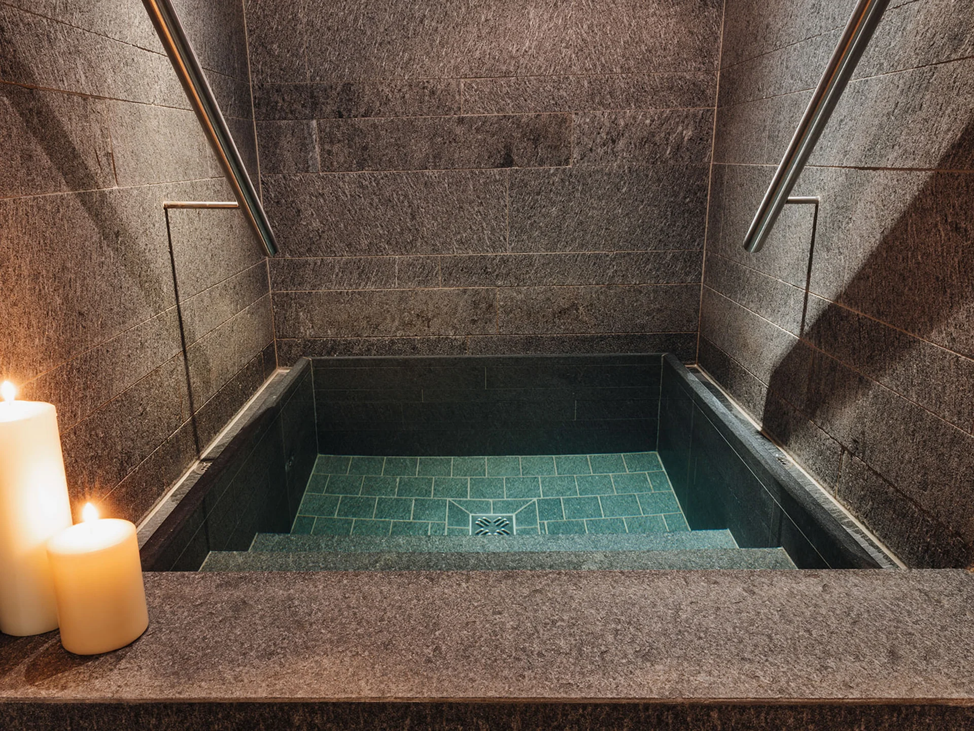Stone stairs leading to a small pool with lit candles on the left