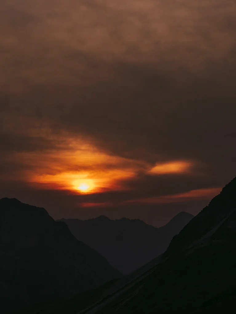 Sonnenuntergang über dunklen Bergsilhouetten mit orangefarbenem Himmel