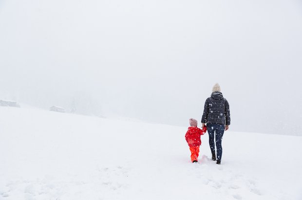 Frau mit Kind machen einen winterlichen Spaziergang während es schneit. 