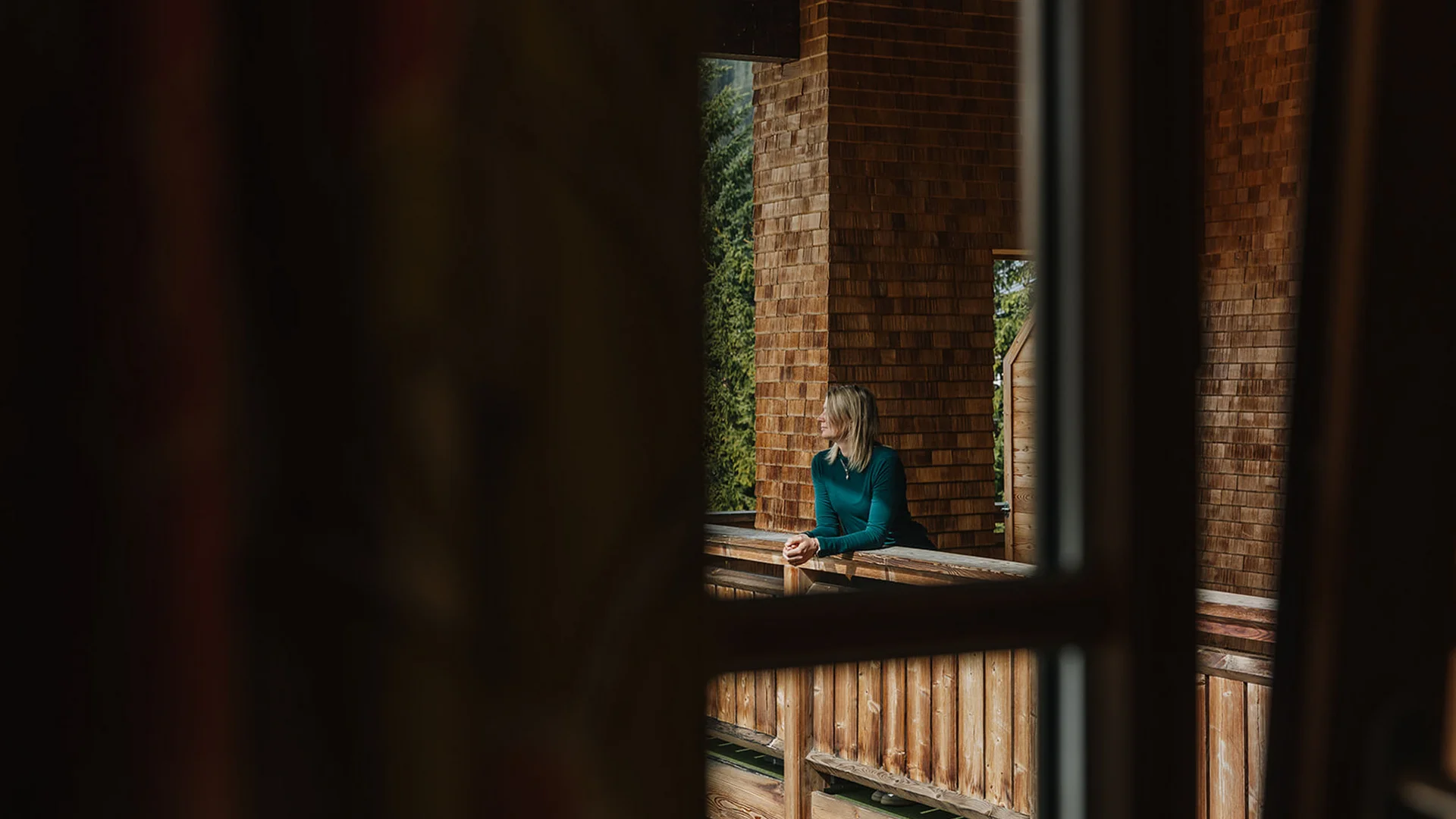 Frau blickt von einem hölzernen Balkon in eine naturnahe Umgebung