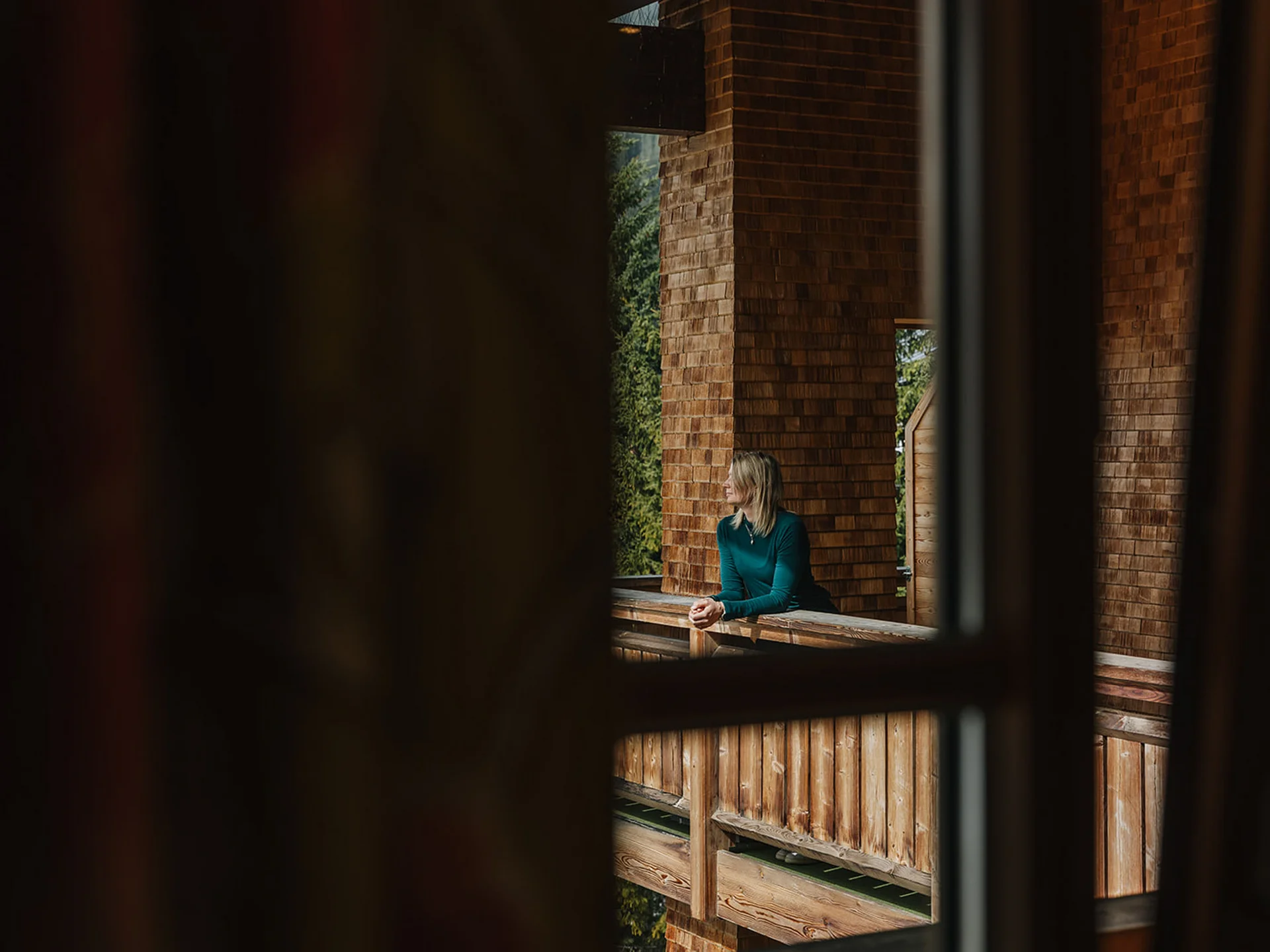 Woman leaning on wooden balcony railing looking into nature