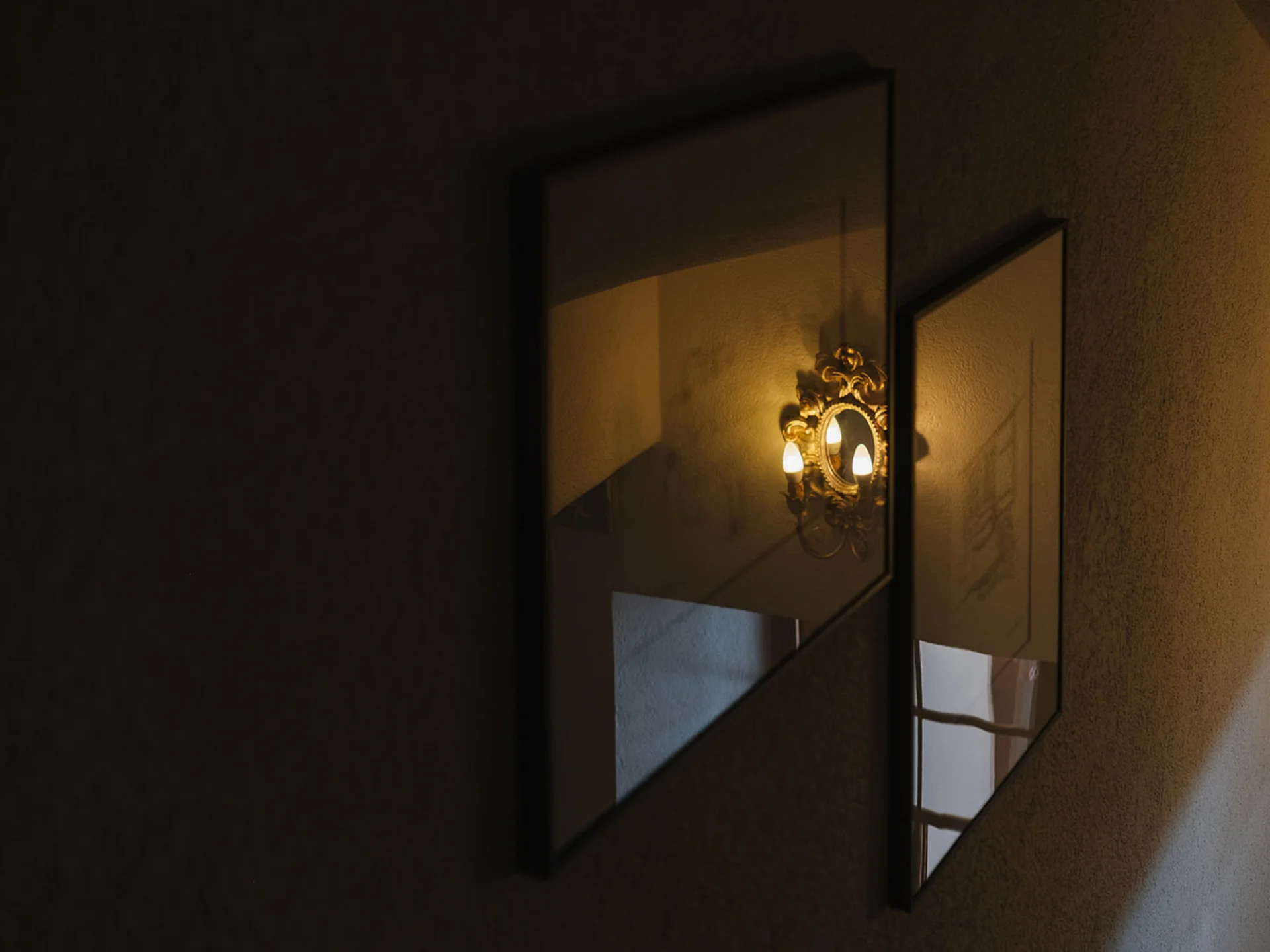 Mirrors reflecting an antique wall lamp on a dark wall