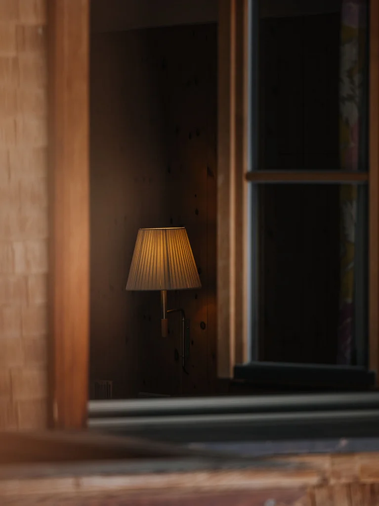 Blick durch ein Fenster auf eine beleuchtete Wandlampe im Innenraum