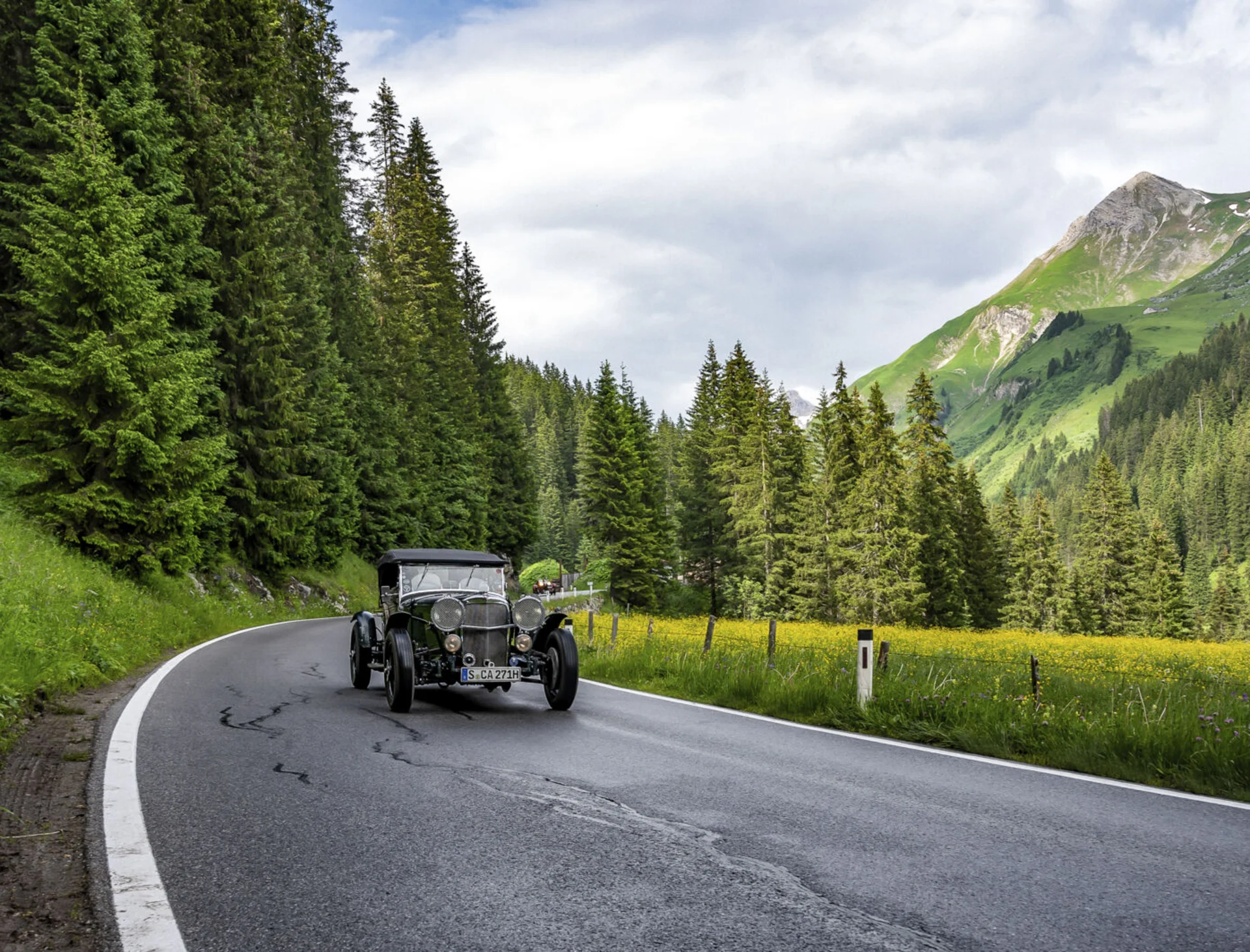 Diverse events set against a stunning mountain backdrop Vintage car driving on winding mountain road surrounded by forest and green meadows