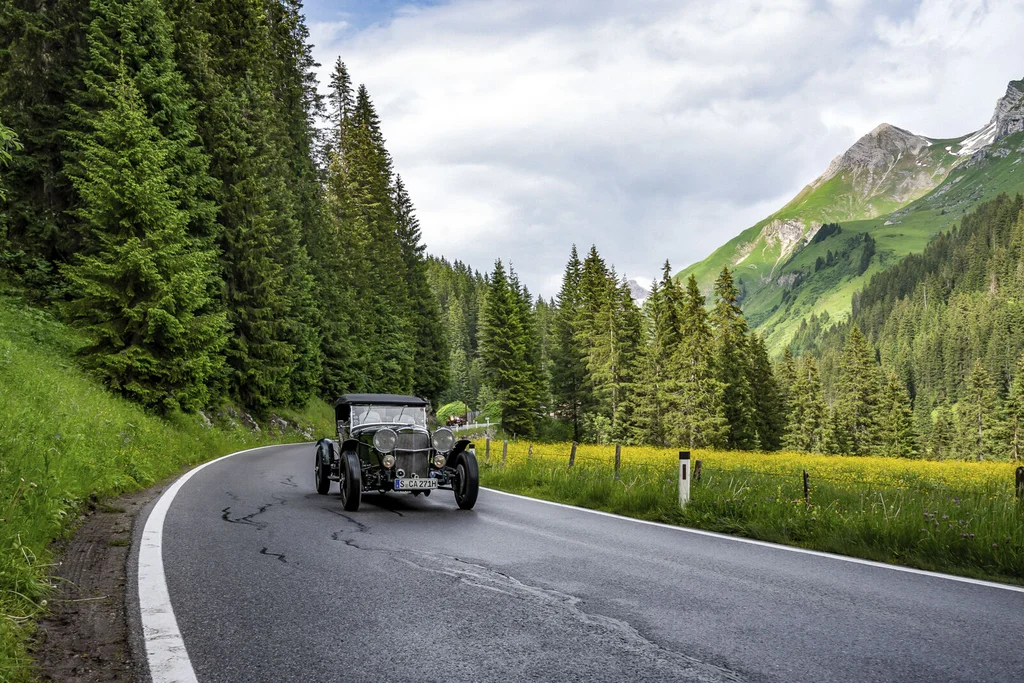 Stories and moments from the Aurora in Lech Vintage car driving on winding mountain road surrounded by forest and green meadows