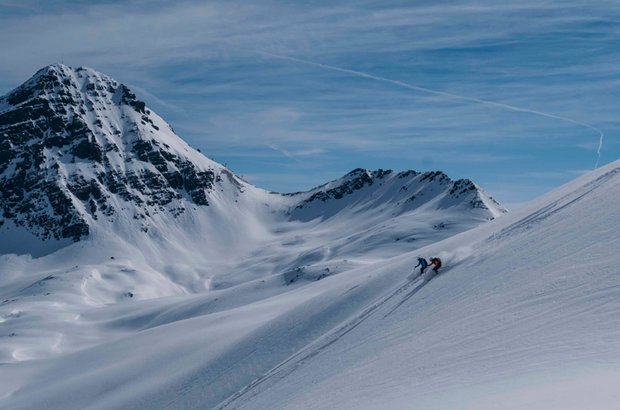 Eine Person fährt mit Ski den verschneiten Hang hinunter