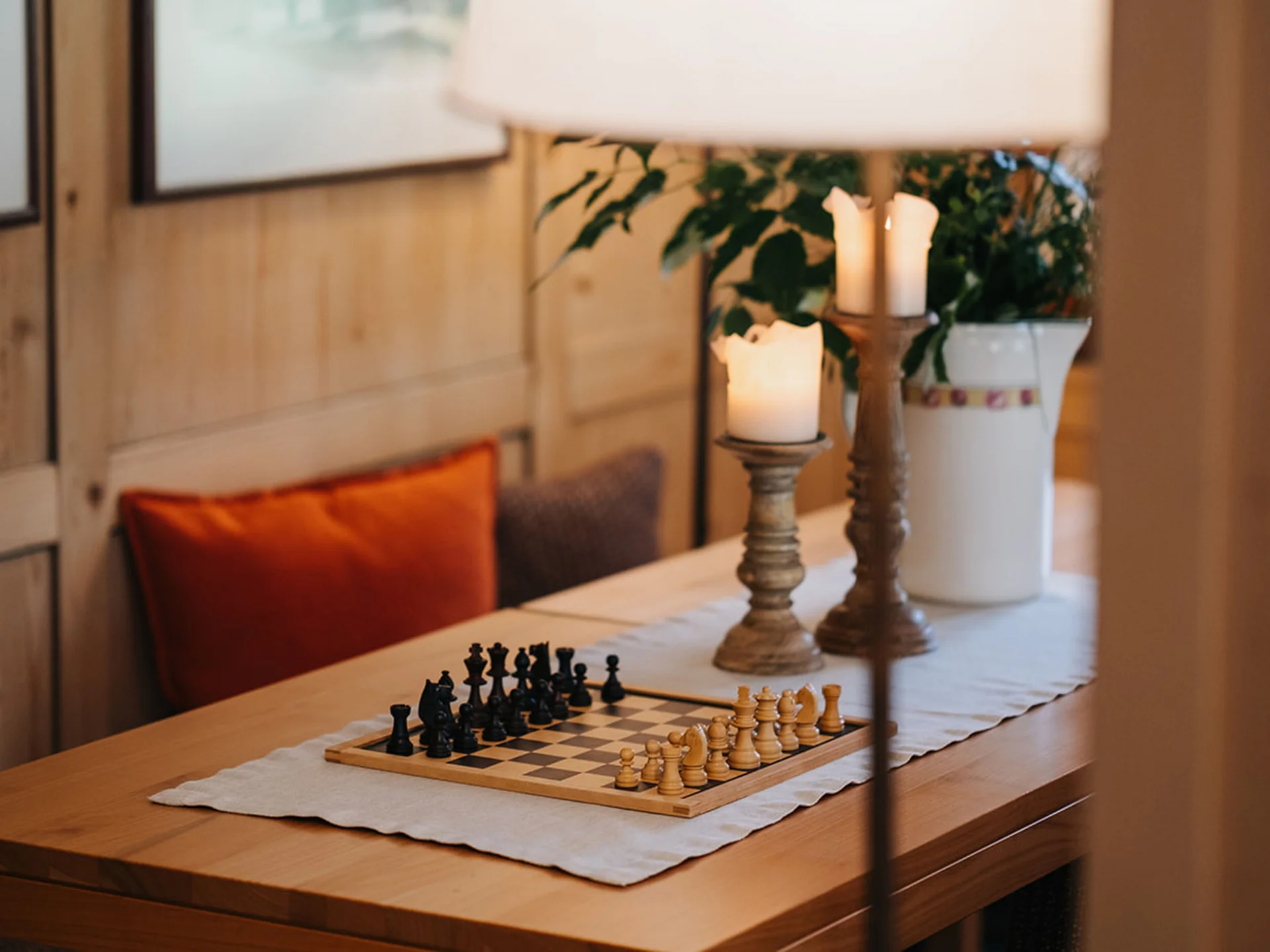 Chessboard on wooden table with candles and cushions in cozy room