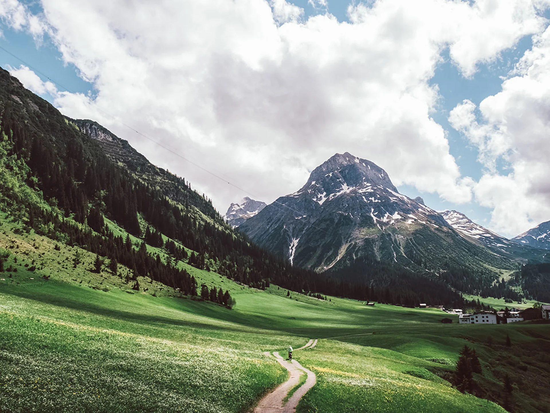 Path through green meadows with mountains and cloudy sky in the background